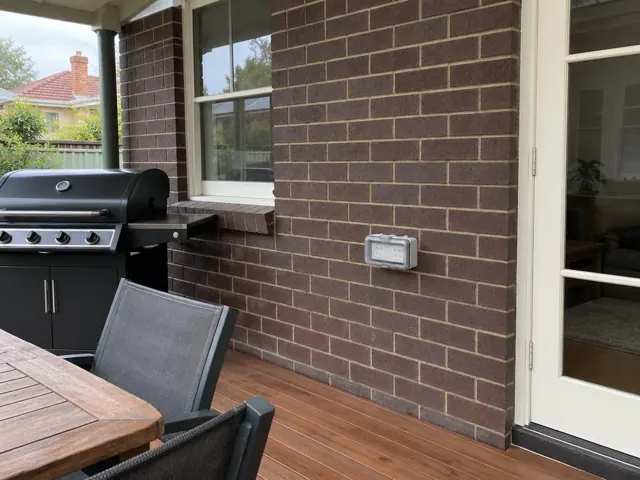 Outdoor power point on a brick wall beside a timber deck and glass door in Waitara